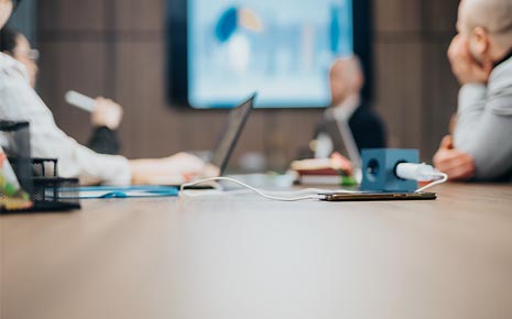 People in a conference room with laptops and phones plugged in on the table